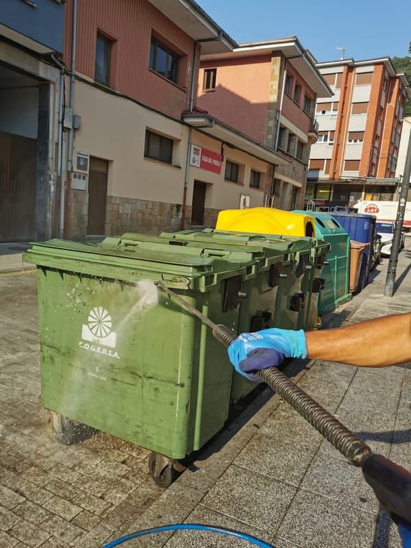 Operario limpiando una batería de contenedores con agua a presión en Lena